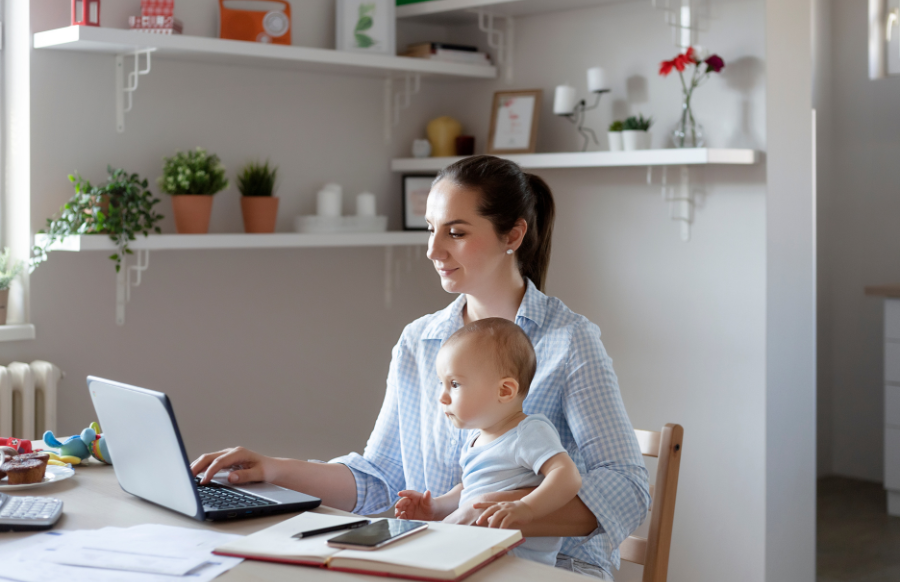 Young mother with baby working at home office on laptop while planning home budget