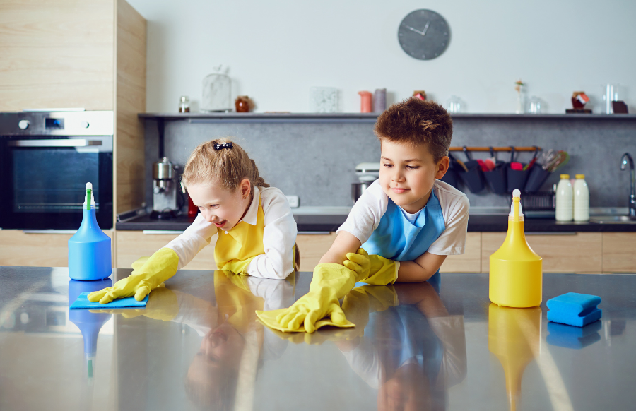 smiling children do the cleaning in the kirtchen counter with detergents and gloves