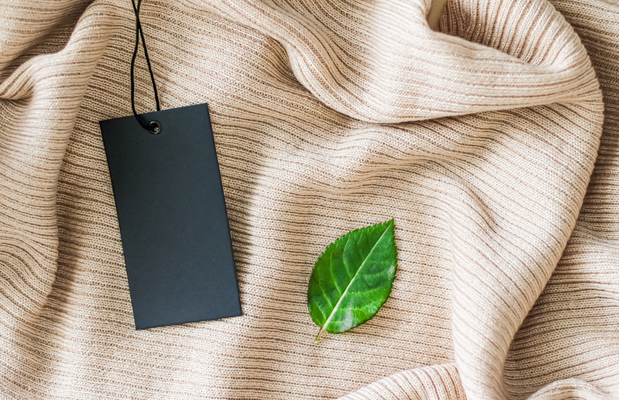 clothing tag and green leaf as eco-friendly flatlay background, sustainable fashion and brand label concept  