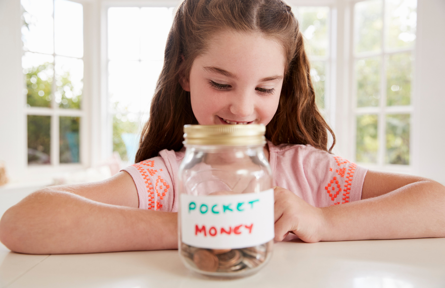 girl saving pocket money in glass jar at home