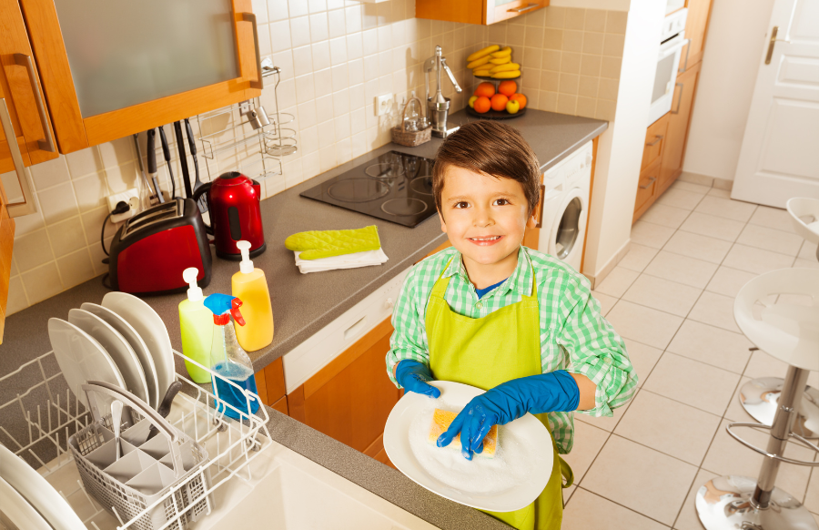 happy little boy wearing rubber gloves washing dishes in the kitchen