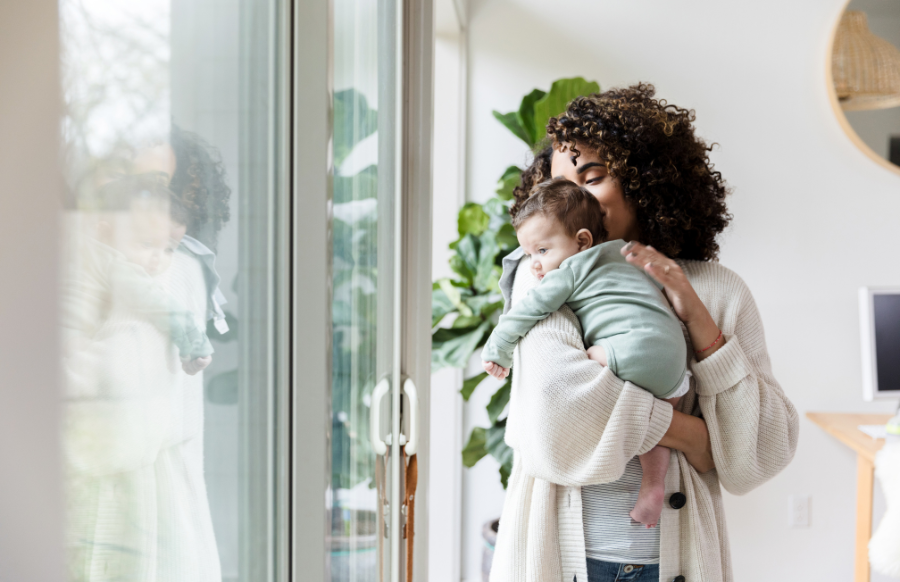 single mother holds her baby while standing by the window in the living room