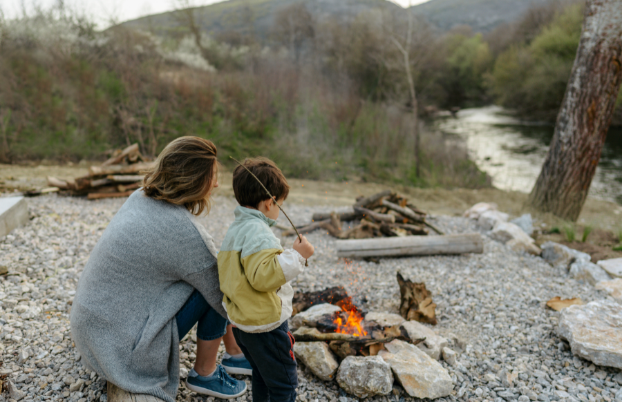 single mother and her boy sitting by the campfire on a riverbank and enjoy beautiful nature