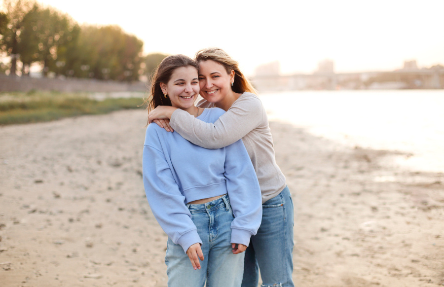 loving mother hugging teenage daughter on shore at sunset