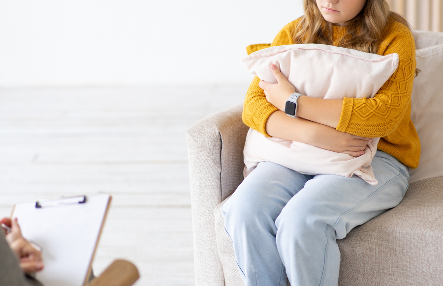 upset and worried teenage girl sits on couch and hugs pillow in a psychotherapy session